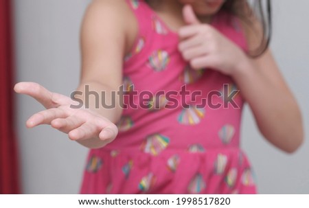 A little girl with pink shirt is giving right hand and left hand showing thumb up. No face seen.