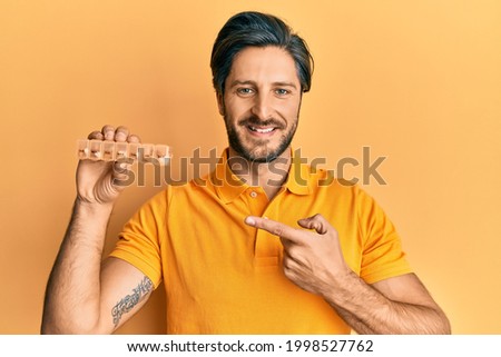 Young hispanic man holding pill organizer smiling happy pointing with hand and finger 