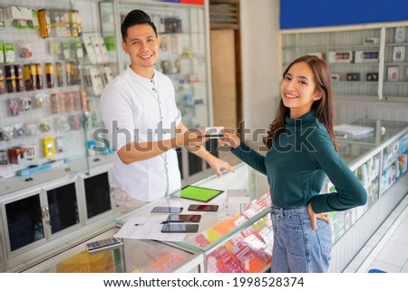 a beautiful woman smiles while giving a credit card to a man when paying at a smartphone shop