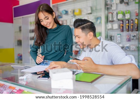 a man and a woman working together checking the records of cell phone accessories against the background of a glass display case in a smartphone shop