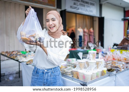 A beautiful girl in a veil buys various kinds of takjil food at a roadside stall Royalty-Free Stock Photo #1998528956