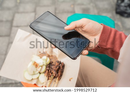 gesture of hand close up taking picture of chicken satay using mobile phone