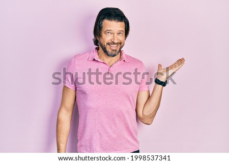 Middle age caucasian man wearing casual white t shirt smiling cheerful presenting and pointing with palm of hand looking at the camera. 