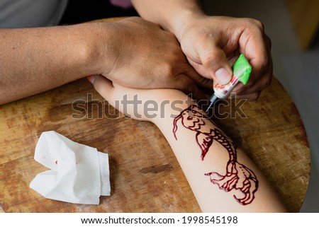 Painting henna ornaments on girl's hand closeup.