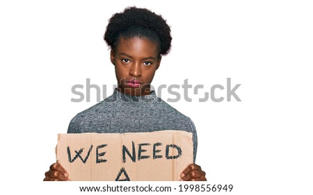 Young african american girl holding we need a change banner thinking attitude and sober expression looking self confident 