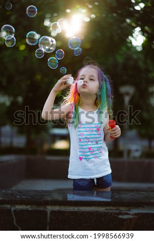 pretty little girl with colorful dyed hair blowing soap bubbles. Saint-Petersburg, Russia.Image with selective focus and backlight