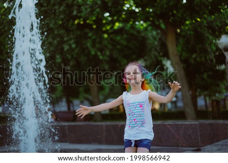 pretty little girl with colorful dyed hair running along fountain parapet with happy smile. Saint-Petersburg, Russia. Image with selective focus