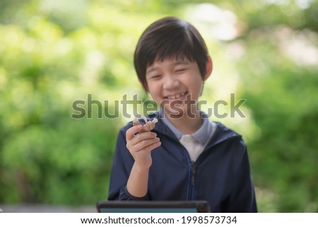 Cute Asian child holding hearing aid on nature background