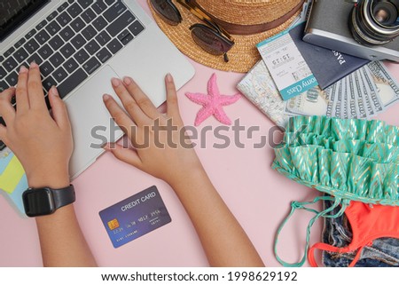Traveler getting ready for a trip, he is packing his bag and booking a flight online using a credit card and a laptop, flat lay. Planning traveling trip notes. travel accessories on pink background.