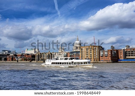 Pleasure boat sailing down the Thames River, London. The Millennium Bridge and St Paul's Cathedral can be seen in the background. Summer day with blue sky and puffy clouds. 