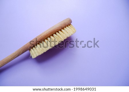Massage brush for the body.  Wooden brush made of cactus fiber on a purple background. Home body care.  Brush for anti-cellulite massage. Photo from above.
