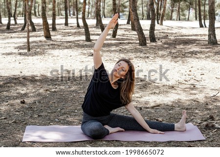A middle-aged female in sportswear stretching on a mat in a park