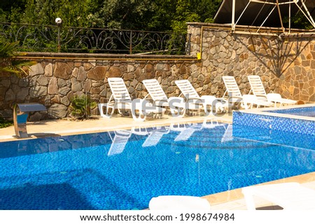 Pool with blue water ladder for descent and ascent into the water. The sun loungers are empty by the pool.