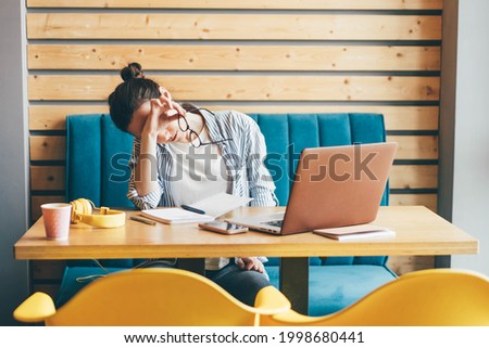 Tired young woman sitting near her laptop at the cafe. Royalty-Free Stock Photo #1998680441