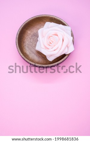 A vertical shot of a pink rose flower in a wooden bowl on a pink surface - beauty and aromatherapy