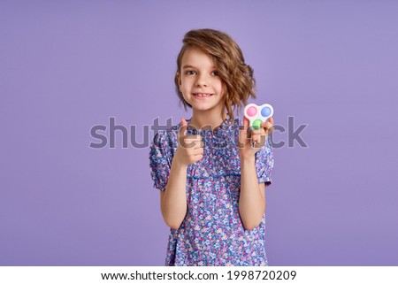 Picture of little girl with a modern popit toy. Colorful and bright pop it toy simple dimple. Trendy anti stress sensory toy fidget push pop it and simple dimple in kid's hands.