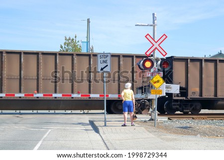 A pedestrian waits as a train passes where signage clearly warns and alerts that it is a dangerous crossing. 
