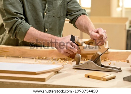 Unrecognizable male joiner work in carpentry using tools. Man is successful entrepreneur at workplace, close-up photo of hands, handmade concept. Workshop on wood. Man create a product made of wood Royalty-Free Stock Photo #1998734450
