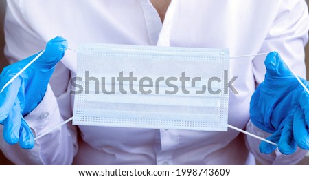 Doctor wear blue disposable gloves holding face mask ready to put it on. Infection prevention concept. Close up cropped image.