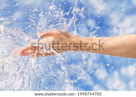 Woman hand with large water splash in it against blue sky. Bright summer image, nature and ecology theme