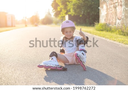 Portrait of little girl in roller skates, sitting on ground.
