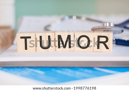 the word tumor is written on wooden cubes near a stethoscope on a paper background. medical concept