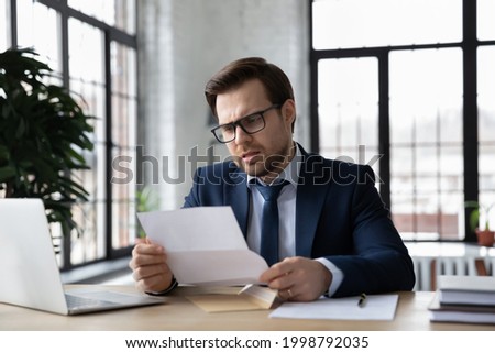 Worried confused businessman reading letter at workplace, holding paper document. Business leader receiving bankruptcy or eviction notice, loan rejection from bank, getting bad news from mail Royalty-Free Stock Photo #1998792035
