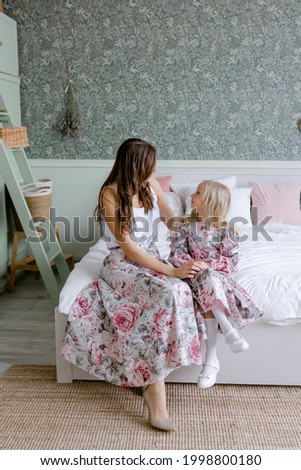 Daughter and mom sit on a white bed in a green scandinavian style bedroom