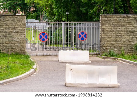 Metal gates with signs "Stop is forbidden" and means of stopping transport in front of them. A stone fence. greens.
