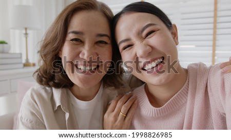 POV attractive beautiful two people asia young lady girl use mobile phone take photo picture video overjoy sit at home sofa couch have good time day together quarantine in mum healthy health care.
