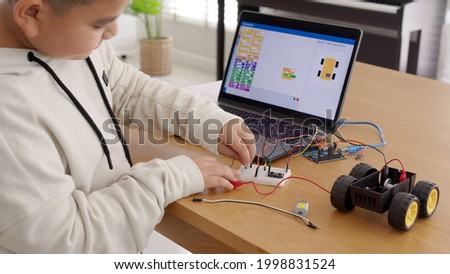 Young asia student remotely learn online at home in coding robot car and electronic board cable in STEM, STEAM, mathematics engineering science technology computer code in robotics for kids concept. Royalty-Free Stock Photo #1998831524