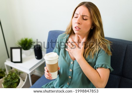 Having a bad reaction to caffeine. Young woman touching her chest and suffering from tachycardia after drinking a strong cup of coffee Royalty-Free Stock Photo #1998847853
