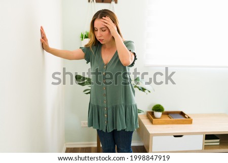 Disoriented woman in her 20s feeling dizzy and trying to balance against a wall background. Sick woman with vertigo illness Royalty-Free Stock Photo #1998847919