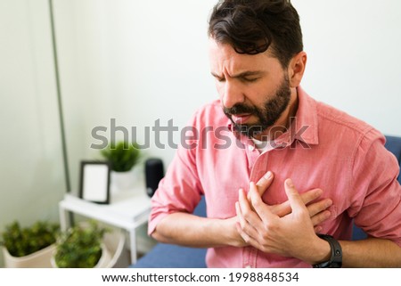 Handsome man in his 30s at home having a heart attack and suffering from chest pain. Middle age man with a cardiovascular disease  Royalty-Free Stock Photo #1998848534