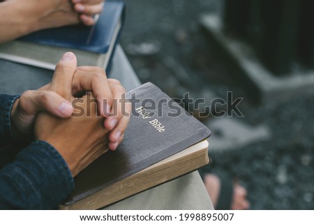 Hands folded praying over a Bible. Casual man praying with his hands together over a closed Bible, Holy Bible in church concept for faith, spirituality, worship, and religion.