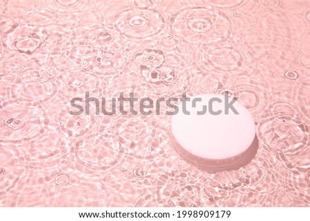 Empty white circle podium on transparent clear pink calm water texture with splashes and waves in sunlight. Abstract nature background for product presentation. Flat lay cosmetic mockup, copy space.