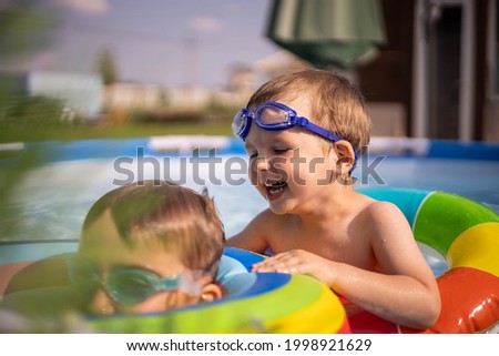 Children in the pool near the house swim and indulge. Two brothers. Little boy and teenager. Blue water and bright swimming circles. Joy, laughter and summer.