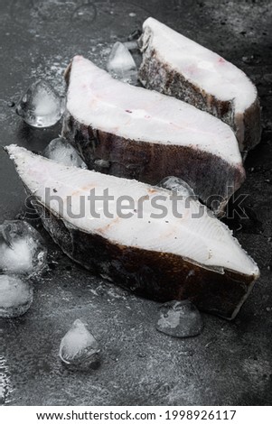 Frozen halibut steak set, on black dark stone table background