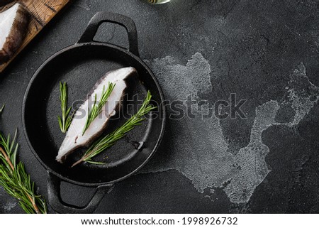 Raw halibut saltwater fish steak set, with ingredients and rosemary herbs, on black dark stone table background, top view flat lay, with copy space for text