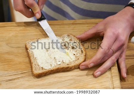 Knife spreading butter on toast bread in womens hands in the morning breakfast. Coffee and dessert concept. High quality photo Royalty-Free Stock Photo #1998932087