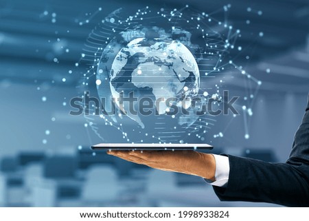 Businessman hand holding tablet with glowing globe interface on blurry office background. Global futuristic innovation concept. Double exposure