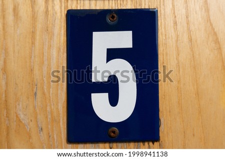old blue enamel sign with white number 5 on a wooden wall