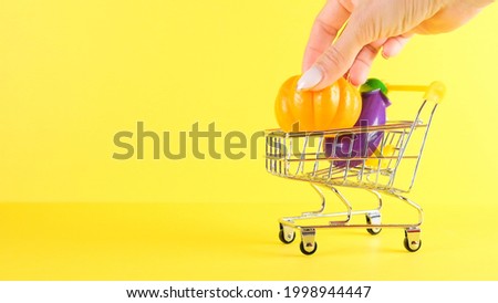 Shopping cart with vegetables inside on a yellow background, closeup. Black Friday Shopping and Discount Concept