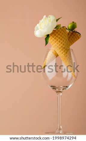 Two waffle cones for ice cream with white peony flowers in a glass glass on a pink background. Festive creative concept for birthday, mothers day, valentines day. Vertical position. Copy space.