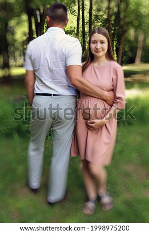 Beautiful young married couple in a love photo session in a summer park. The wife and husband are expecting a baby and are happy together.