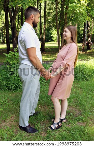 Beautiful young married couple in a love photo session in a summer park. The wife and husband are expecting a baby and are happy together.