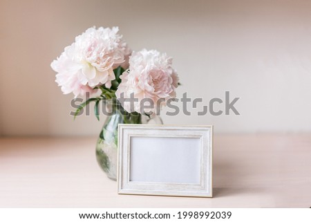 Portrait white picture frame mockup on wooden table. Modern glass vase with peony. White wall background. Scandinavian interior.	