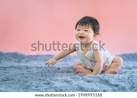Asian baby smiling and sitting on carpet with pink color background. Cute 6 months baby sitting with copy space use as concept of valentine, love, learn, education, baby or kid department in hospital. Royalty-Free Stock Photo #1998995168