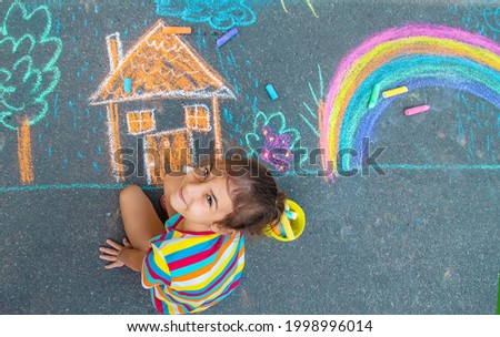 The child draws a house and a rainbow on the asphalt with chalk. Selective focus. Kids. Royalty-Free Stock Photo #1998996014