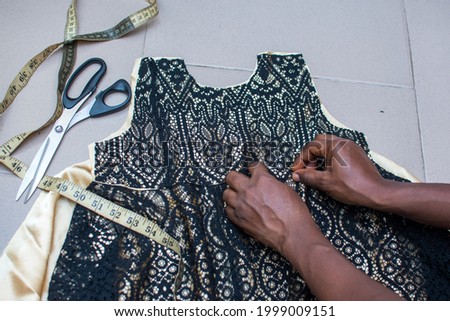 An African fashion designers hands working on a dress, fabric or clothe with a tape measure and scissors to get the best output as a tailor